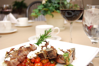 Lamb chops with tomatoes and rosemary on a white plate on a restaurant table.